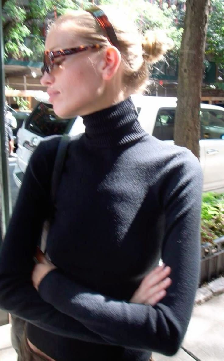 Carolyn Bessette-Kennedy in a black turtleneck and sunglasses on a city sidewalk