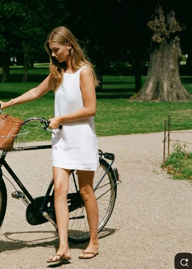 Woman in a plain white shift dress and flat sandals beside a bicycle showing how restraint can make a simple look feel stronger