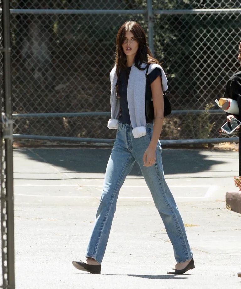 Kaia Gerber in jeans, flats, a shoulder bag, and a tied sweater