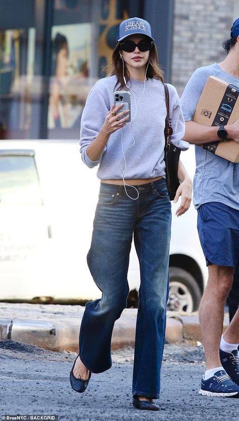 Woman in a grey sweatshirt, dark jeans, ballet flats, sunglasses, and a baseball cap showing an outfit that feels inhabited rather than over-managed